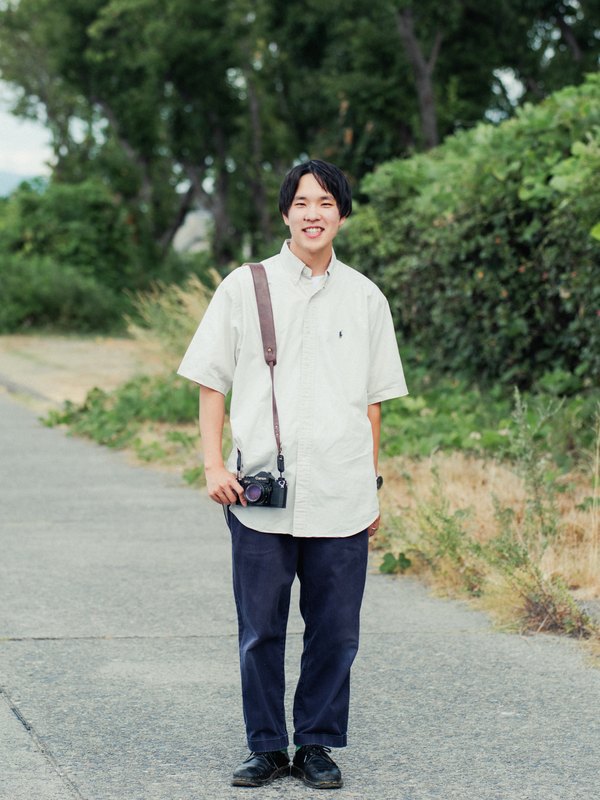 カメラを提げて立つ代表・藤本惇平